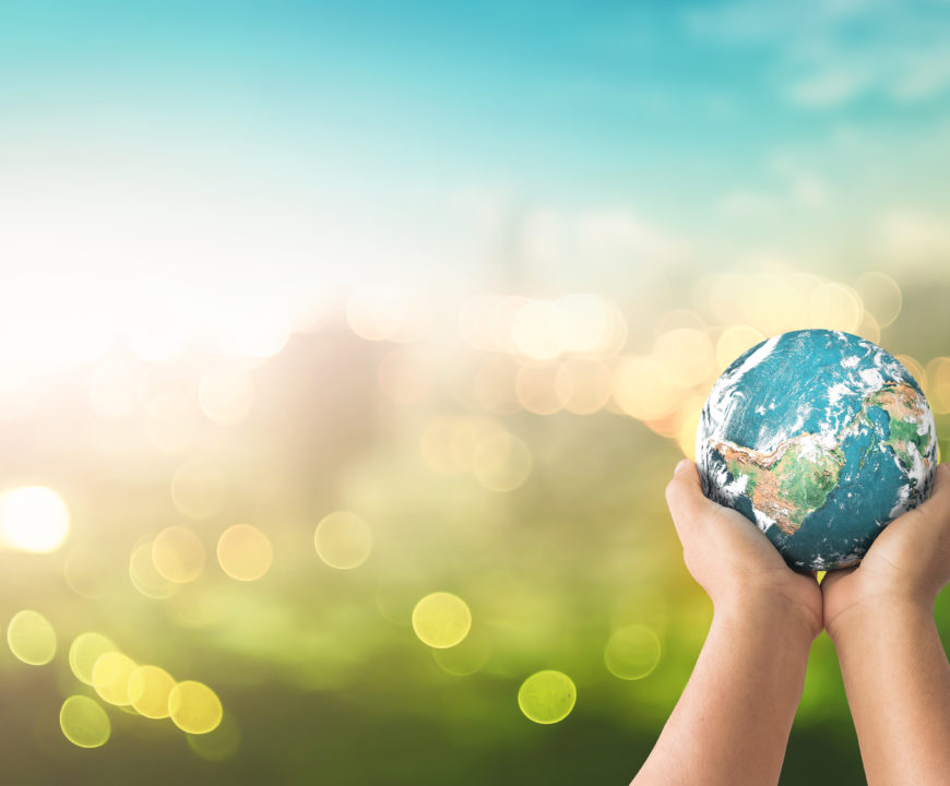 A pair of hands gently holding up a miniature Earth globe.